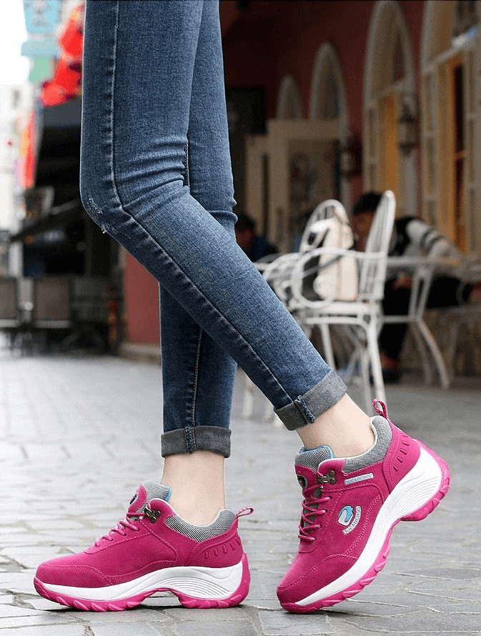 Woman wearing pink fur-lined sports sneakers paired with jeans, showcasing insulated and stylish suede design in an urban setting.